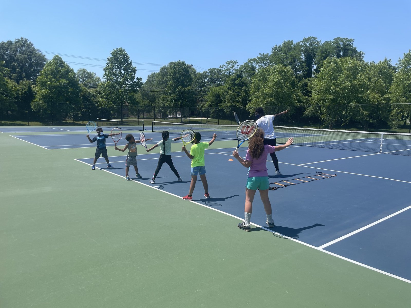 Kids practicing forehands with a coach at an outdoor Miles Ahead Foundation youth clinic